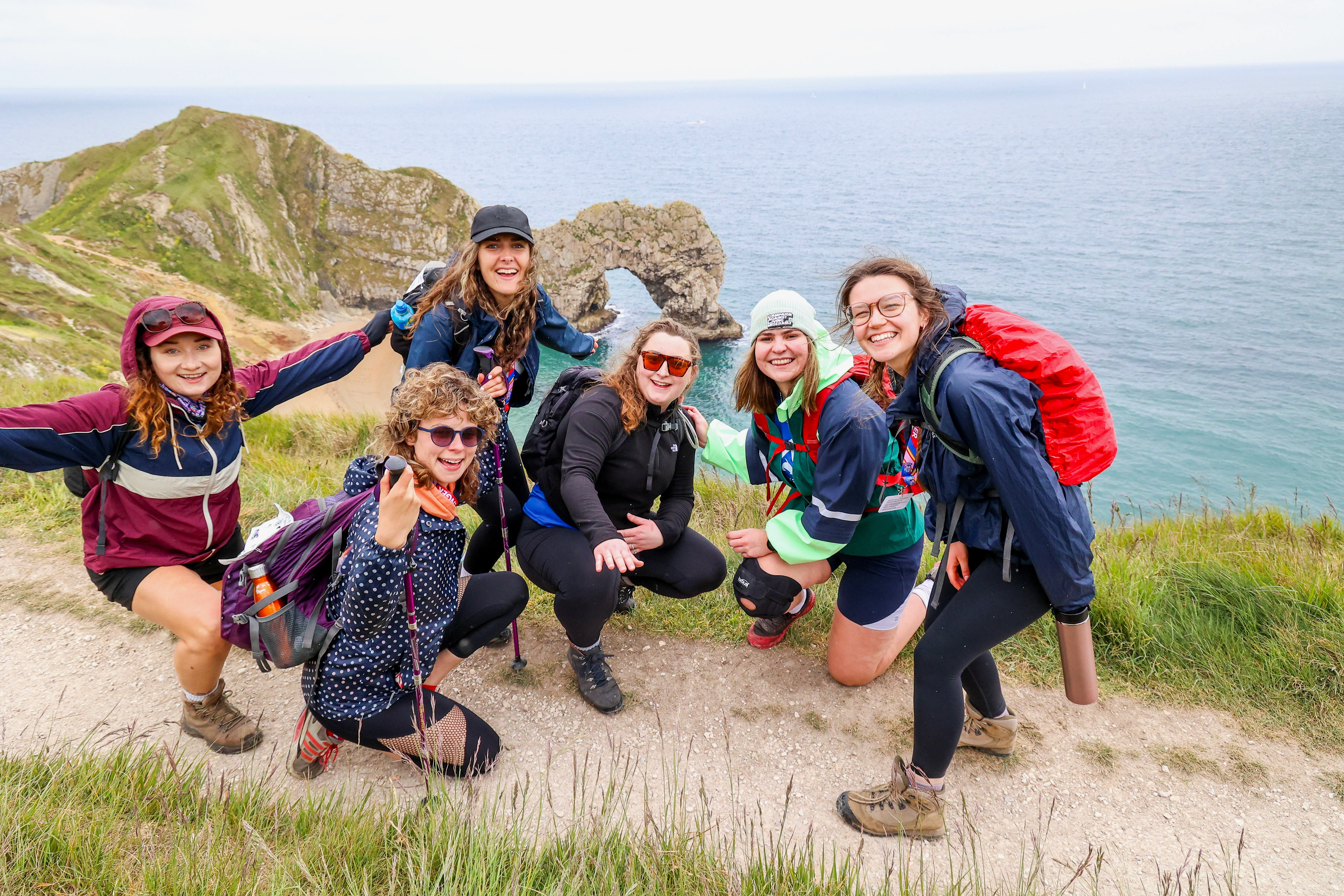 A group of six Jurassic Coast Ultra Challenge participants along the cliffs next to Durdle Door. They are smiling, wearing outdoor gear and rucksacks.
