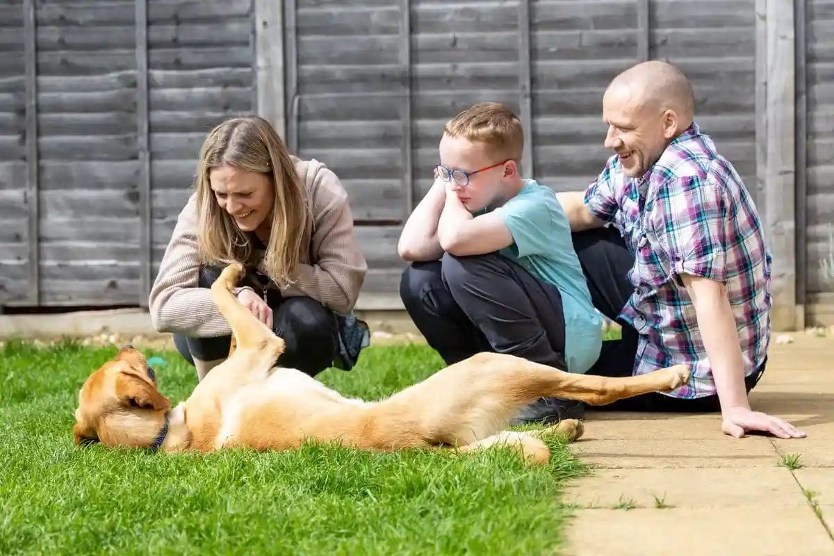 Family Dog Golden Retreiver Laying Down Grass Garden Child Parents Sat Down Smiling Frontfacing