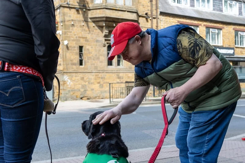 Man holding dog lead and stroking dog's head smiling by the side of the road